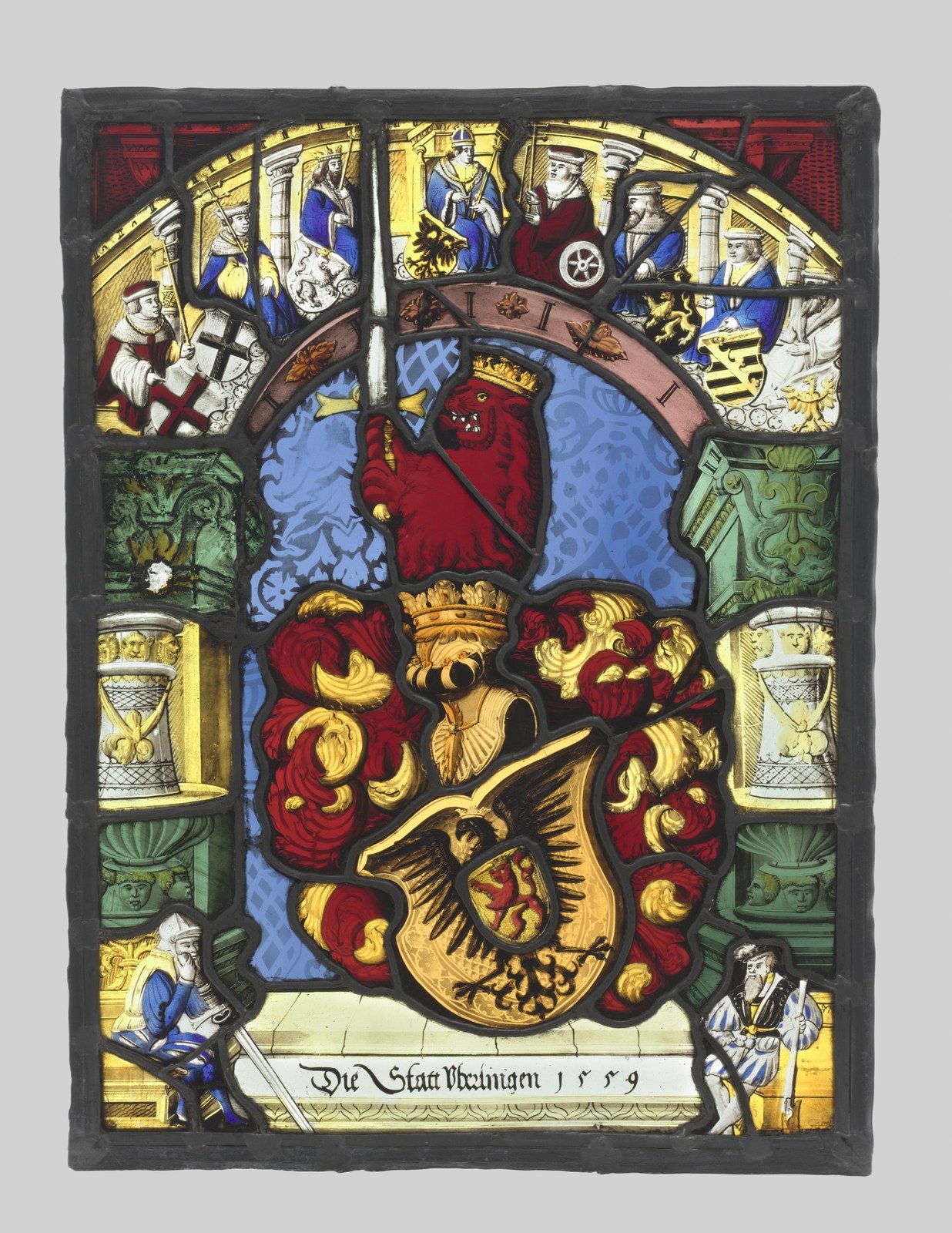 A large yellow shield with a dark eagle occupies the lower centre beneath a helmet and curling ornament. A red lion with a sword appears above, framed by columns and a populated arch.