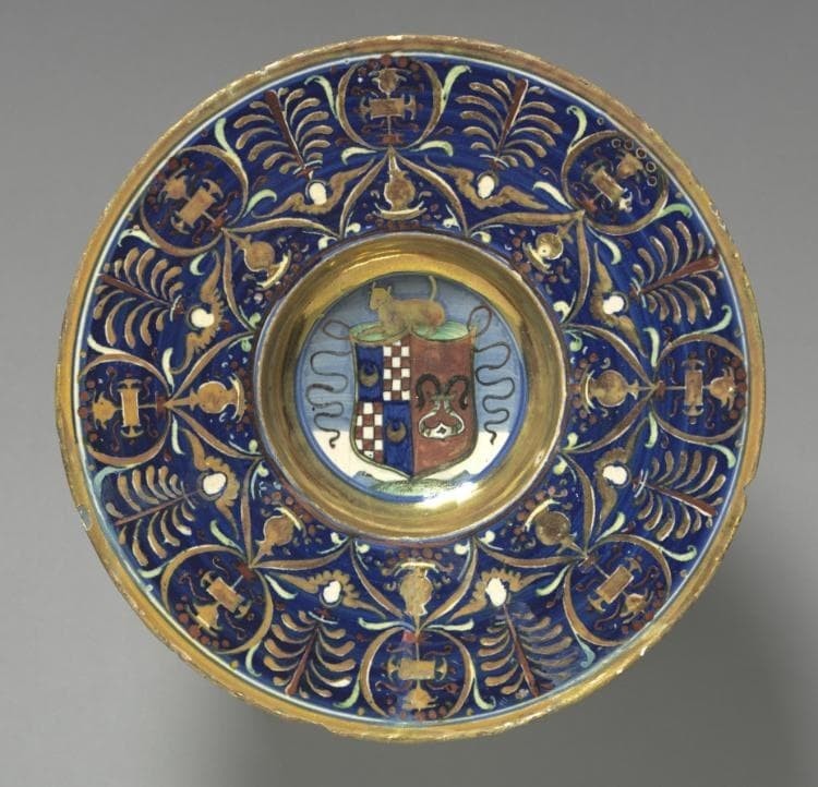 An Italian plate with a blue and gold ornamental rim and a central shield containing checked compartments, crescent shapes, and a red area; an animal appears above the shield.